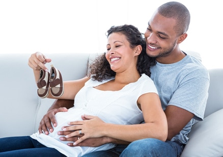 man dangling baby shoes in front of pregnant woman