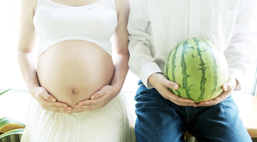 men holding small watermelon next to pregnant woman