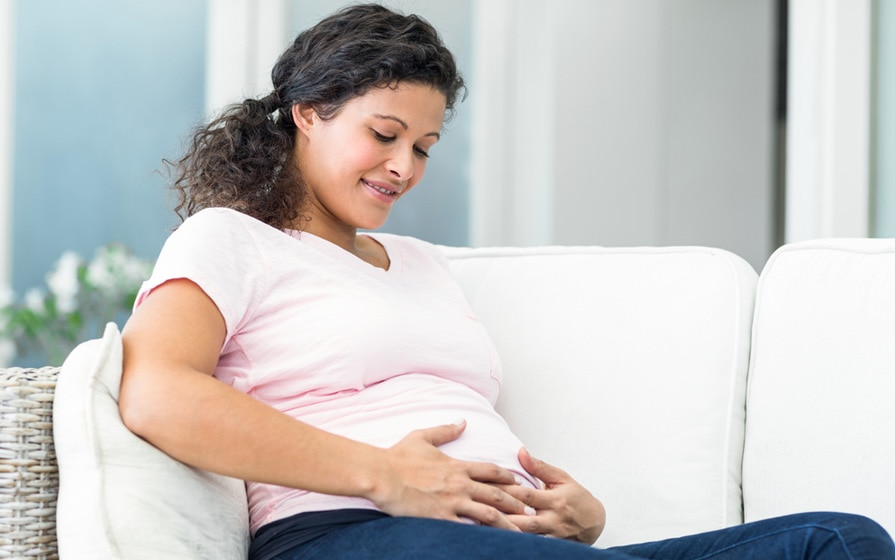  women on couch holding pregnant belly