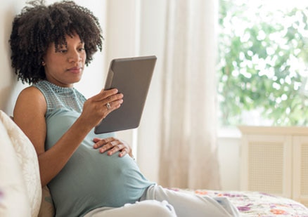 pregnant woman reading an iPad while lounging on her bed
