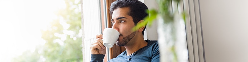 young man drinking coffee looking out window